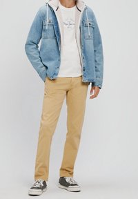 Veste en denim bleu clair avec doublure en polaire blanche, chinos beige et baskets grises avec semelles blanches. T-shirt blanc avec détail logo.
