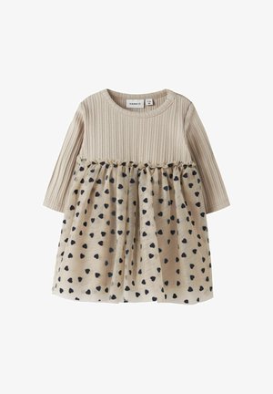 Robe à manches longues avec un haut beige à côtes et une jupe beige ornée de motifs en forme de cœur noirs, agrémentée d'une couture froncée à la taille.