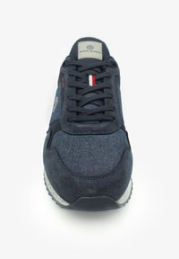 Donkerblauwe sneaker met textiel bovenwerk, vetersluiting, grijze rubberen zool, voorzien van een klein logo op de zijkant en rode/witte accentstrepen.