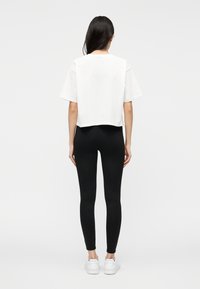 T-shirt branca corta com mangas curtas, combinada com leggings pretas e ténis brancos. Design simples e limpo, sem padrões ou detalhes visíveis.