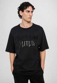 Melnas kokvilnas T-krekls ar brīvu piegriezumu, ar reljefiem burtiem "Versace Jeans Couture" kontrastējošā apdarē priekšā.