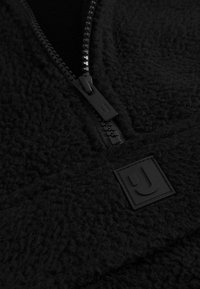 Pullover in pile nero con zip liscia e tessuto strutturato. Include un'etichetta logo quadrata nera e un aspetto morbido e accogliente.