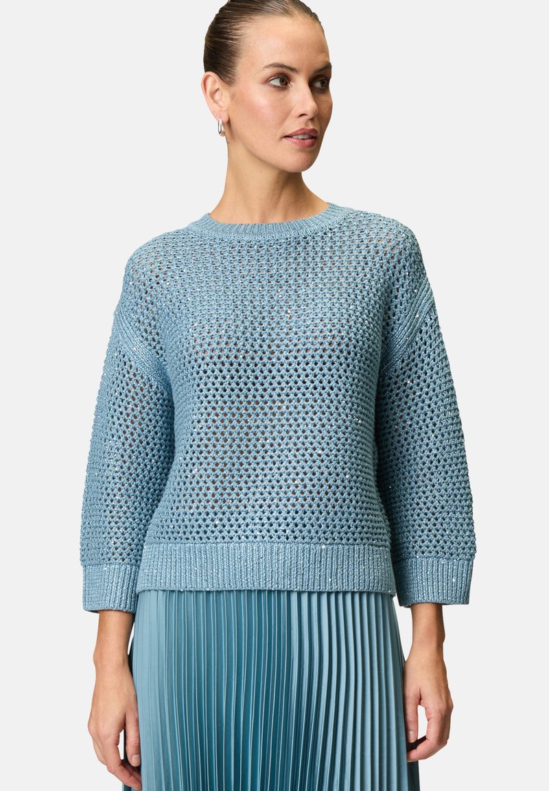 Maglione azzurro chiaro a maglia, con una trama ampia e aperta, caratterizzato da un collo rotondo e maniche a 3/4, abbinato a una gonna blu plissettata.