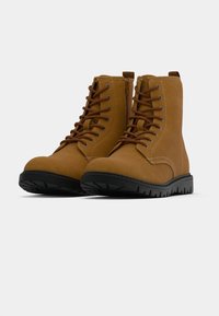 Brązowe zamszowe botki za kostkę z brązowym wiązaniem, bocznym zamkiem błyskawicznym, czarną gumową podeszwą i wytrzymałym bieżnikiem zapewniającym przyczepność.
