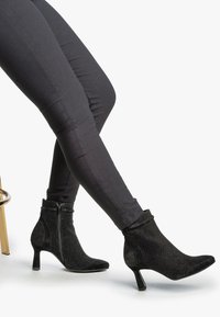 Botines negros de tobillo que presentan una mezcla de tejido texturizado y ante suave, adornados con pequeños detalles de tachuelas y un tacón de altura media.