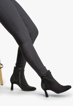Black ankle boots featuring a mix of textured fabric and smooth suede, adorned with small stud details and a mid-height heel.