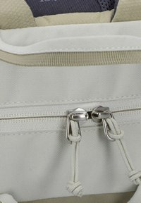 Weißer Stoff-Rucksack mit einem oberen Reißverschluss und silbernen Metallgriffen, akzentuiert durch einen beigen Rand und eine strukturierte Oberfläche.