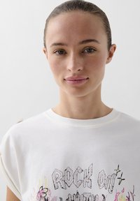 White cotton t-shirt featuring "ROCK ON" text in patterned letters, with floral and star designs. Short sleeves with rolled edges.