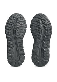 Suole in gomma nera scanalate di un paio di scarpe sportive del marchio Asics, viste dal basso.