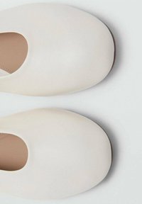 Zapatos de piel blanca, tipo slip-on, con punta redondeada y superficie lisa. Diseñados sin hardware ni patrones visibles. Suela delgada y plana.