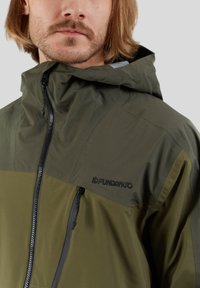 Jacket w kolorze oliwkowym z kapturem, posiadający dwukolorowy design, wytrzymały materiał, zamek błyskawiczny z przodu oraz logo na klatce piersiowej. Gładka tekstura.