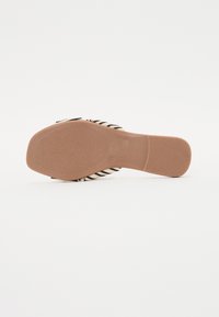 Svart og beige stripete sandal med glipper, featuring en teksturert såle og en glatt, brun såle, designet for enkel påføring.
