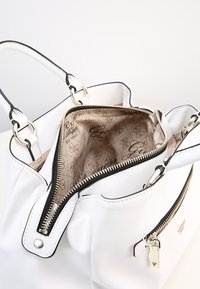 Biała skórzana torebka z czarnymi akcentami, zamkiem błyskawicznym u góry, srebrną metalową biżuterią i wzorzystym beżowym wnętrzem z logo. Płaski design.