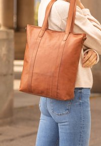 Brun läderhandväska med två långa remmar, vertikala sömnadsdetaljer och en mjuk textur. Väskan har en minimalistisk design.