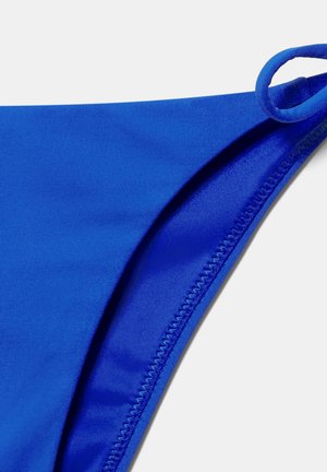 Donji dio badića od plavog tkanog materijala s bočnim remenom u obliku petlje i vidljivim šavovima na bijeloj pozadini.