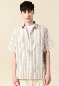 Korte mouwen shirt in beige met verticale zwarte strepen. Voorzien van een knoopsluiting aan de voorkant en een ontspannen pasvorm. Textuurstof.