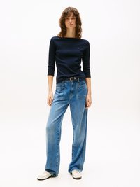 Mørkeblå langermet topp med rund hals, kombinert med vide lyseblå jeans. Modellen har på seg hvite joggesko med subtil merking på toppen.
