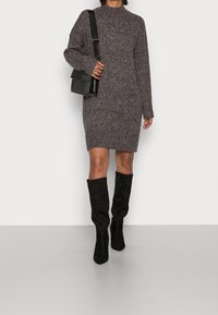 Abito maglione in grigio scuro con collo alto, maniche lunghe e vestibilità comoda. Abbinato a stivali al ginocchio in suede neri e una borsa piccola.