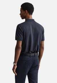 Tmavomodré polo tričko s jemnou textúrou, krátkymi rukávmi a klasickým golierom, kombinované s tmavými šitými nohavicami a čiernym opaskom.