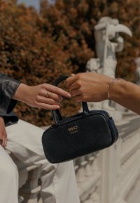 Geantă de mână din piele neagră, cu un design structurat, formă rectangulară, branding auriu și două mânere superioare, ținută de două mâini.