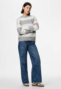 Randig stickad tröja i vitt och grått, med rund halsringning. Matchad med högmidjade, löst sittande blå jeans och avslappnade sneakers.