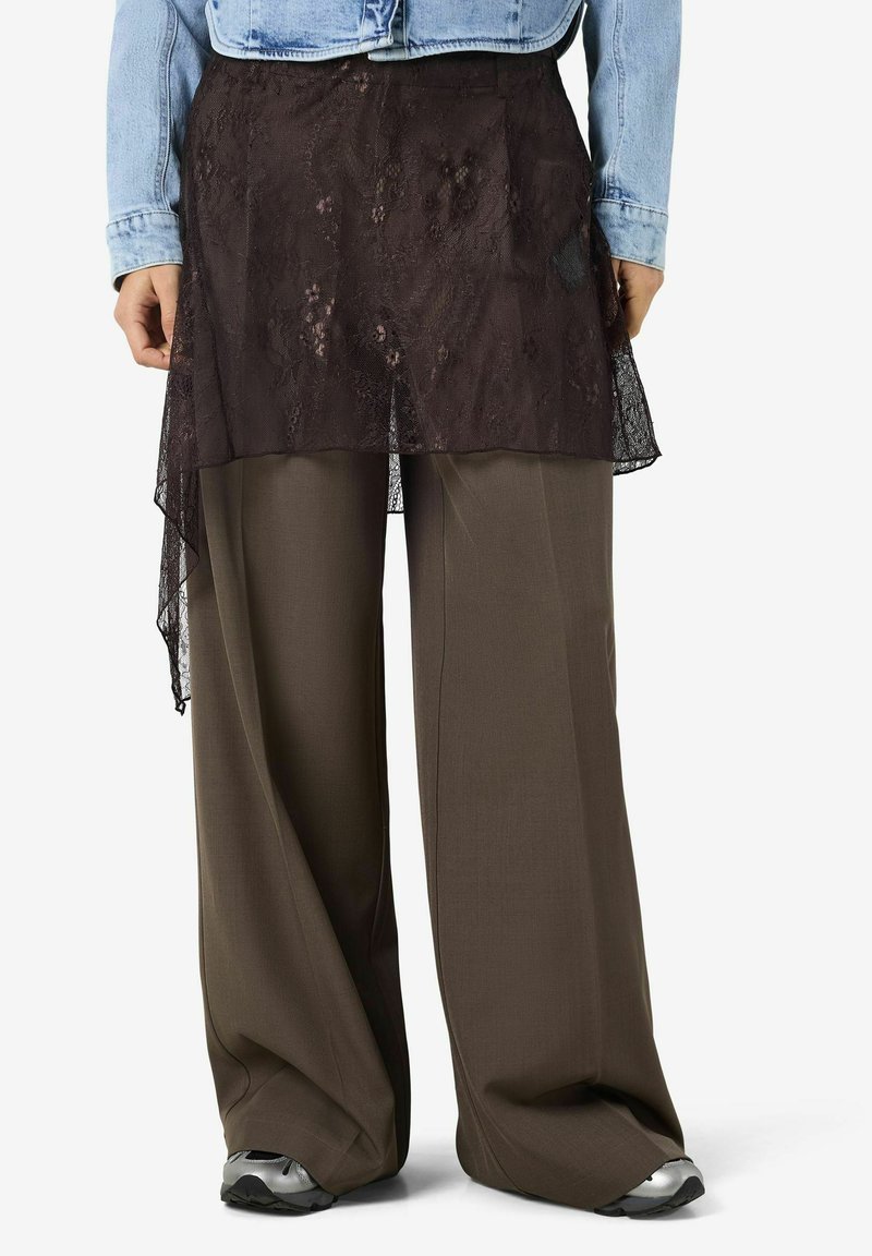 Mustast pitsist tõmblukuga seelik, mis on kihtidena laia lõikega tumedate pruunide pükside kohal, millel on sile tekstuur, kõrge-lage serv ja peen lillemotiiv.