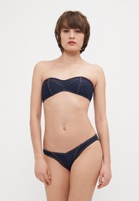 Denim bikinin komplet v temno modri barvi. Brez naramnic zgornji del z oblikovanimi skodelicami in kontrastnim šivom. Bikini spodnji del z nizkim pasom in minimalno pokritostjo.