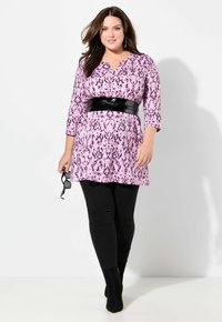 Tunic a fantasia rosa con scollo a V e maniche 3/4, cincta in vita con una cintura nera lucida, abbinata a leggins neri e stivaletti.