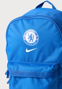 Kék hátizsák tartós anyagból, kör alakú Chelsea Football Club logóval és egy Nike pipa jellel. Cipzáras záródások és állítható pántok.