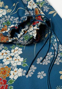 Tissu bleu avec des motifs floraux blancs, rouges, orange et verts et un détail froncé avec un cordon et de longues attaches bleues.