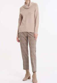 Beige, ribbstickad tröja med polokrage tillsammans med bruna rutiga byxor. Byxorna är åtsittande med linjer i olika färger. Beige boots med blockklack.