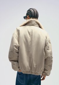 Könnyű bélelt dzseki műszőrme gallérral, elasztikus derékkal és látható varrásokkal. Kék farmeranyag fölé viselve, laza fazonnal.