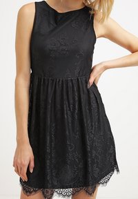 Black dress with a textured floral pattern, sleeveless design, gathered waist, and lace trim at the hem.