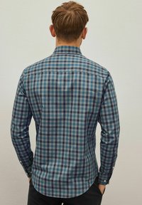 Camisa de manga larga, abotonada en un patrón de cuadros azul y verde con cuello, que presenta un dobladillo curvado y puños de un botón. La tela tiene una textura suave.