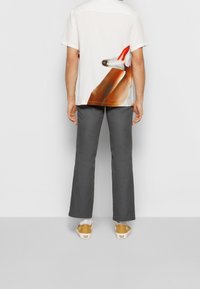 Valkoinen lyhythihainen paita, jossa on värikäs eläinkuvio selässä, yhdistettynä harmaisiin housuihin ja keltaisiin kenkiin.