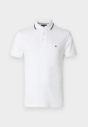 Polo blanc en coton, avec un col bordé de noir, une patte à trois boutons, et un petit logo brodé sur la poitrine.