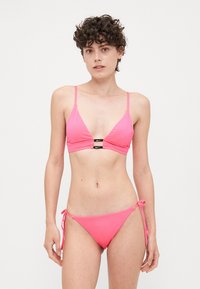 Roze bikini set met een driehoekige bralette met dunne bandjes en een sluiting aan de voorkant, gecombineerd met bikini broekjes met zijstrik. Glad textuur.