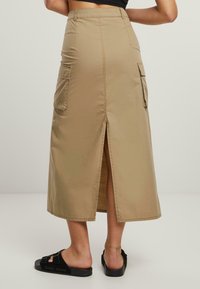 Khaki midi-hame, joka on valmistettu sileästä kankaasta ja jossa on sivutaskut, takatuuletus sekä istuva vyötärö, mikä luo rentoa siluettia.