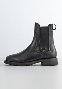 Schwarze Leder Chelsea-Stiefel mit elastischen Seitenpaneelen, runder Zehenform, niedrigem Blockabsatz, grünem Schlaufenanhänger und goldfarbenem Logo-Detail an der Seite.