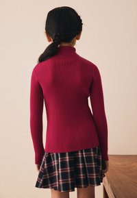 Maglione a collo alto aderente color magenta con costine, abbinato a una gonna svasata a quadri blu navy. L'outfit presenta maniche lunghe e una finitura testurizzata.