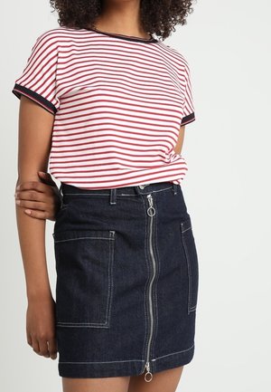 Frau trägt ein rot-weiß gestreiftes Kurzarmshirt, das in einen dunklen Jeansrock mit vorderem Reißverschluss und großen aufgesetzten Taschen gesteckt ist.