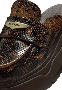 Brązowy wsuwany but o fakturze skóry węża z błyszczącym wykończeniem, wyposażony w złotą metkę "AIR JORDAN" i grubą, ciemną gumową podeszwę.