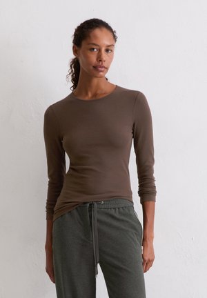 Braun langärmliges T-Shirt in taillierter Form, aus weichem Stoff, kombiniert mit grauen Jogginghosen mit Kordelzug und mit Reißverschlusstaschen.