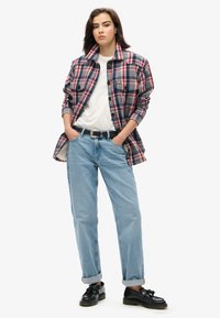Rød, blå og hvidternet flannel-skjorte, båret over en hvid t-shirt. Lyseblå lige ben jeans og sorte loafers fuldender outfittet.