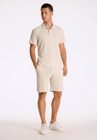 Kort beige frottépiké och matchande shorts, med en klassisk krage, korta ärmar och sidofickor. Matchas med vita sneakers.
