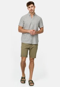 Camisa de manga corta a rayas en gris y blanco, pantalones cortos caqui y sandalias verdes. La camisa presenta un cuello abotonado y rayas verticales.