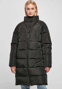 Cappotto trapuntato nero con colletto alto, caratterizzato da sezioni a righe orizzontali, tasche laterali e una cerniera a tutta lunghezza. Tessuto liscio e lucido.