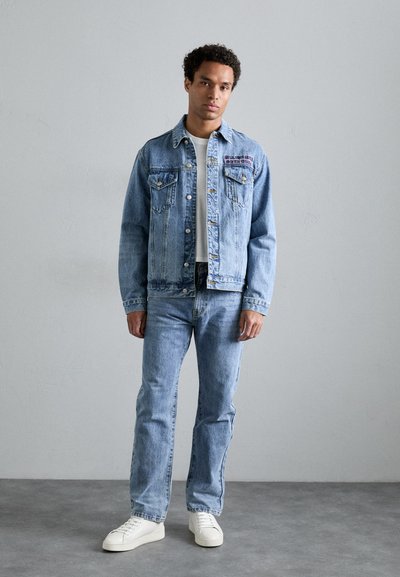 Lichtblauwe denimjacket met frontzakken en geborduurde details, gecombineerd met bijpassende jeans en witte sneakers. Soepele textuur, casual pasvorm.