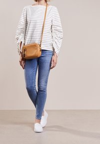 Biały top w paski z bufkami, niebieskie obcisłe dżinsy i białe wsuwane buty. Mała jasno-brązowa torebka na ramię dopełnia strój.