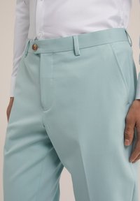 Light blue trousers made of smooth fabric, featuring a fitted design, side pockets, and a single button closure at the waist.